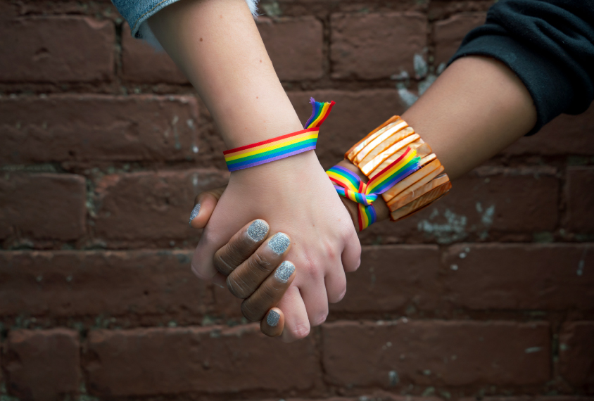 Close-up of two hands holding and wearing rainbow-striped bracelets.