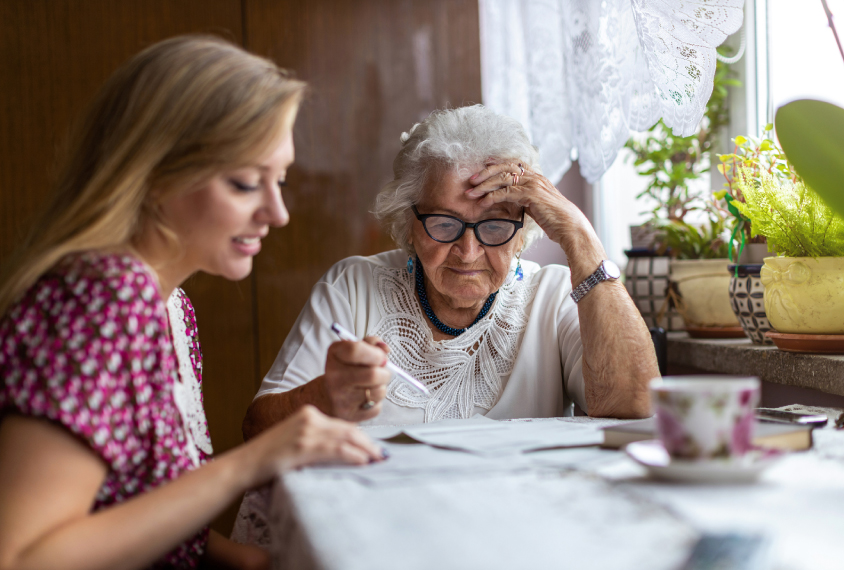 Photograph shows young woman and older woman discussing paperwork.