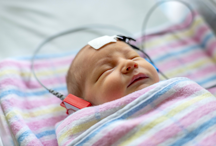Infant in hospital blankets undergoes a hearing test.