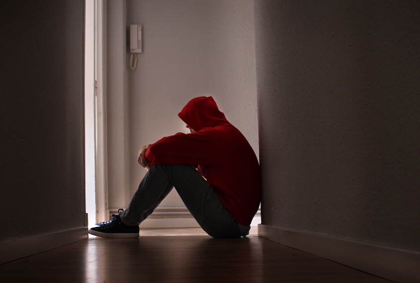 Depressed teenager sitting on floor in darkened hallway.