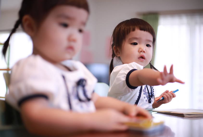 Approximately 24 month old twin girls, one of them reaching for something.