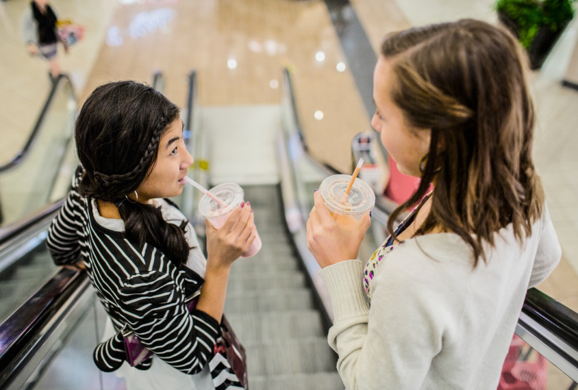 Two teen girls talking on an escalator.