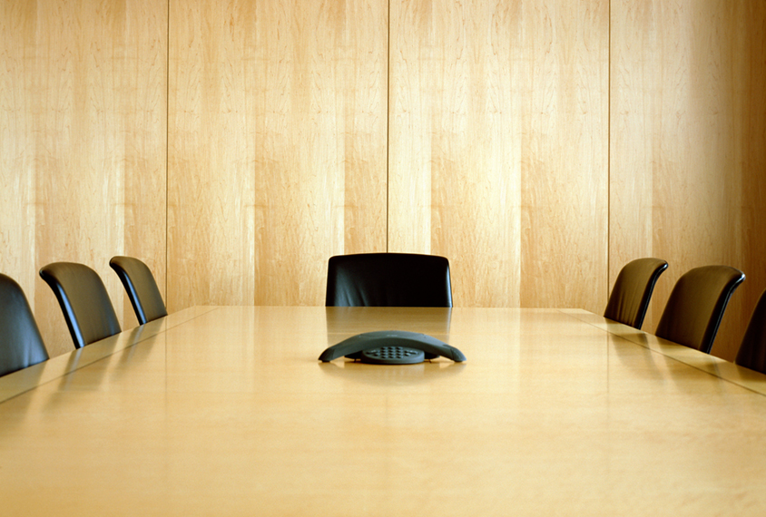an empty conference room paneled in light colored wood, with 7 empty chairs and a conference phone.