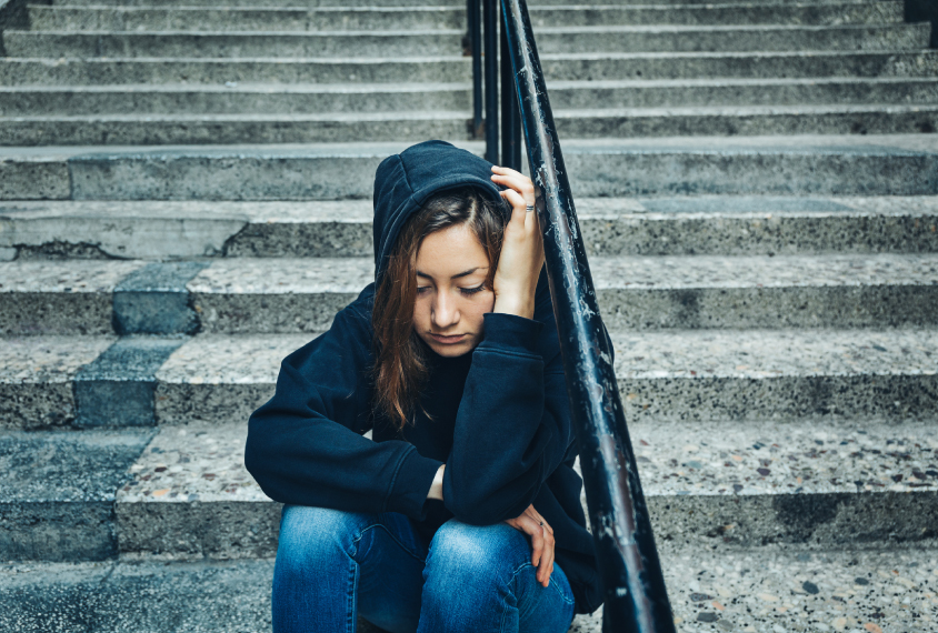 young woman sitting on steps alone, looking anxious.