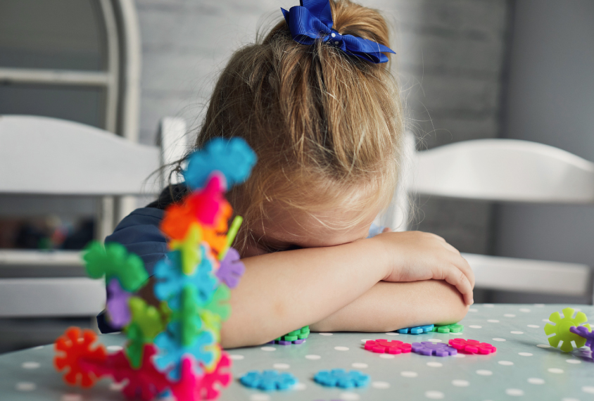 Young child sitting at table with head down, asleep.