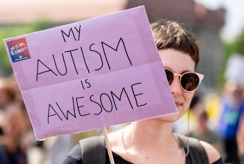 Woman at protest holding sign which says, "My Autism is Awesome"