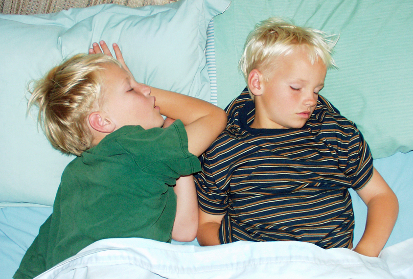 Twin boys sleeping on green sheets.