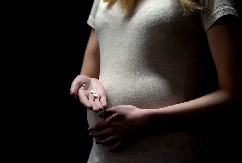 Pregnant woman holding two white pills in her hand.