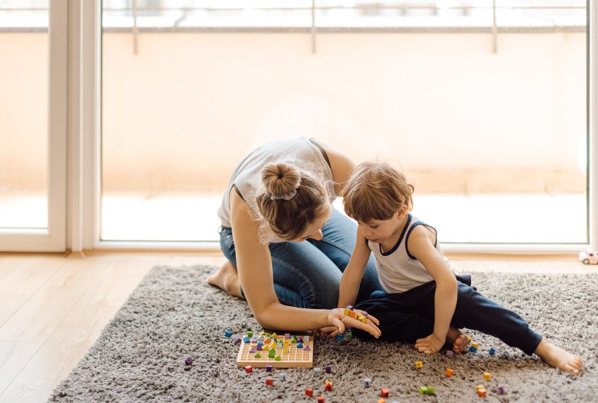 Mother and child playing with small colored blocks on the carpet.