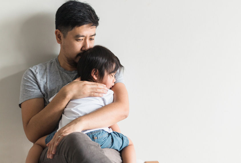 A concerned man holds his toddler close