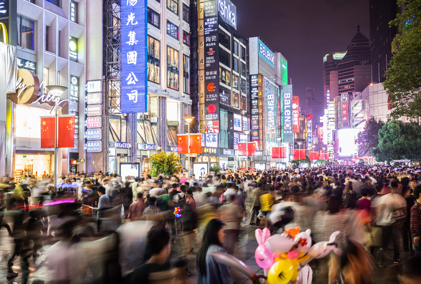 Nighttime crowded Shanghai street scene with illumination from electric and neon signs.