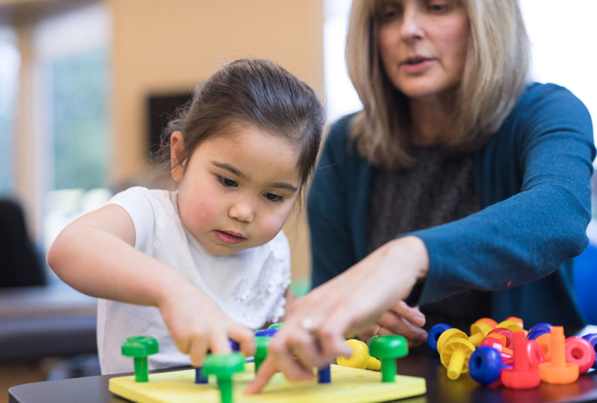 Child with colorful tactile puzzle and clinician or therapist.