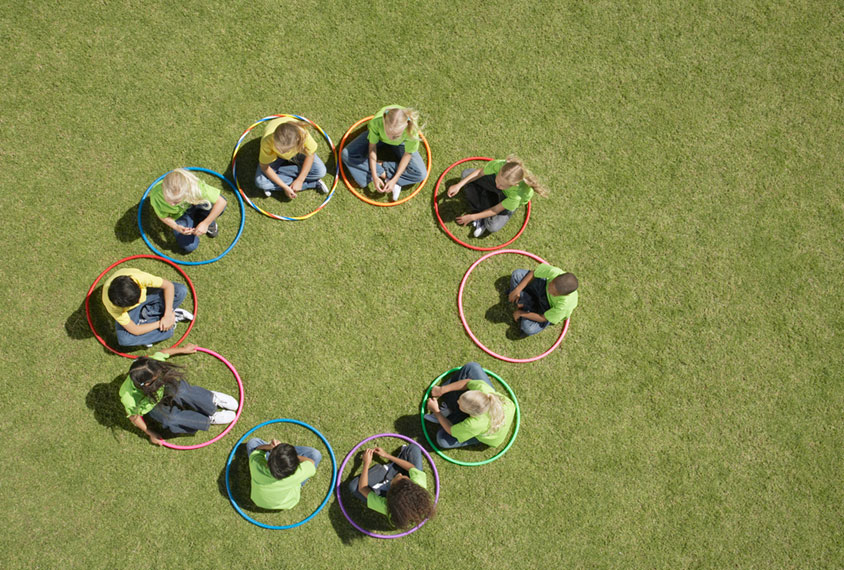 Birds-eye-view of children sitting on grass in a circle formation each inside a hula hoop to represent improved identification and diagnosis of autism.