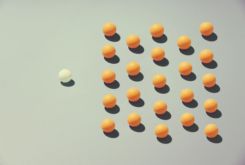 One white ball next to a large group of orange balls.