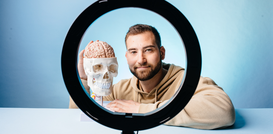 Dr. Ben Rein seen through the circle of a ring light with a skull and brain model.