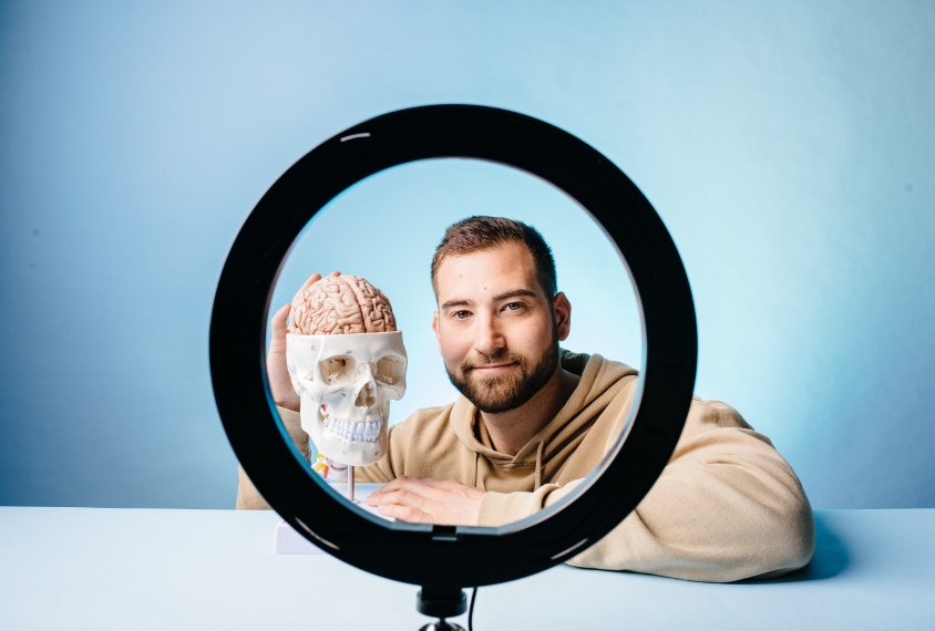 Dr. Ben Rein seen through the circle of a ring light with a skull and brain model.