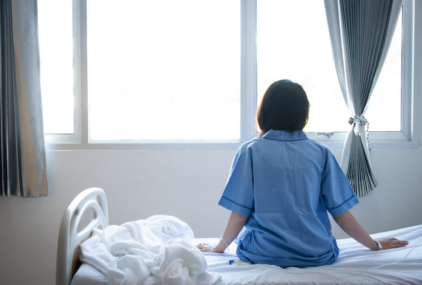 Woman sits on a hospital bed and looks out of a window.