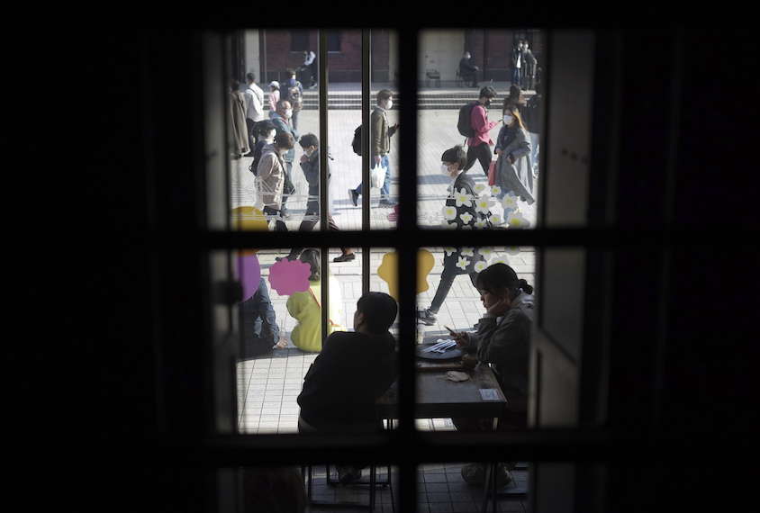 Two people in cafe seen through window, crowded street beyond.