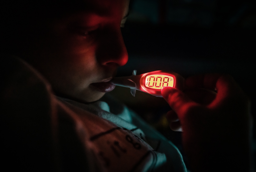 Child in dark room with thermometer showing 100.8.
