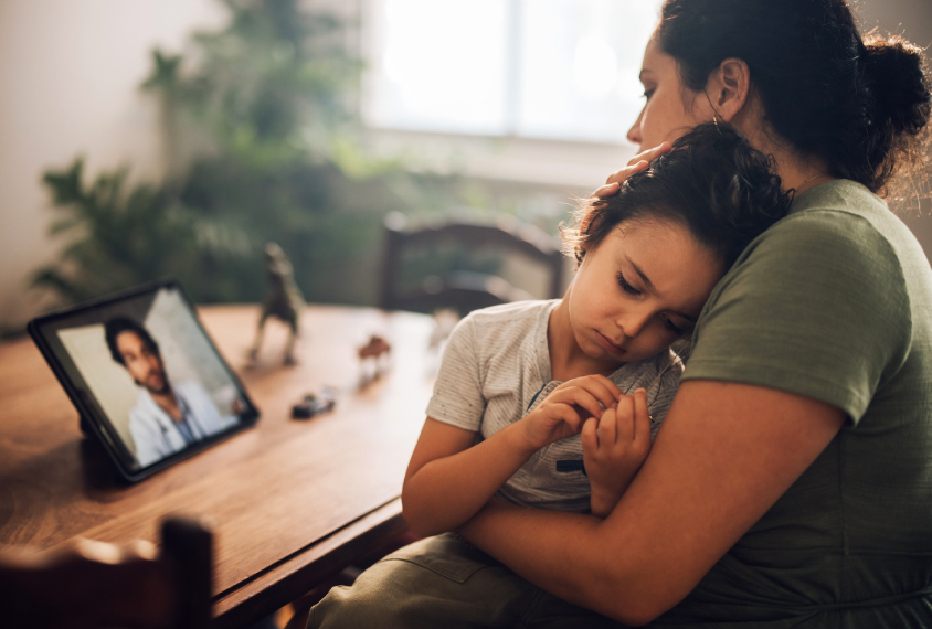 A mother holds her son while on a video call with a doctor.