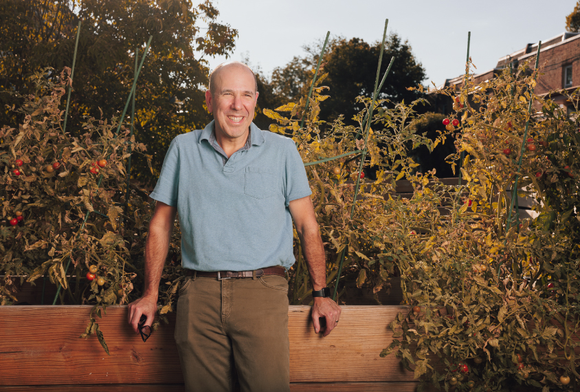 Autism researcher David Mandell smiling and leaning against a wall next to a tomato garden.