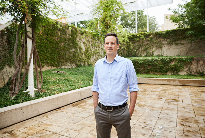 Noah Sasson, a thin white man, stands in a courtyard with his hands in his pockets.