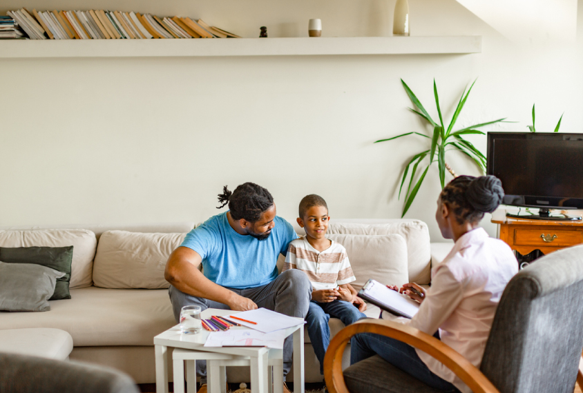 A father and son sit on a couch while a neuropsychologist sits across from them in an armchair.