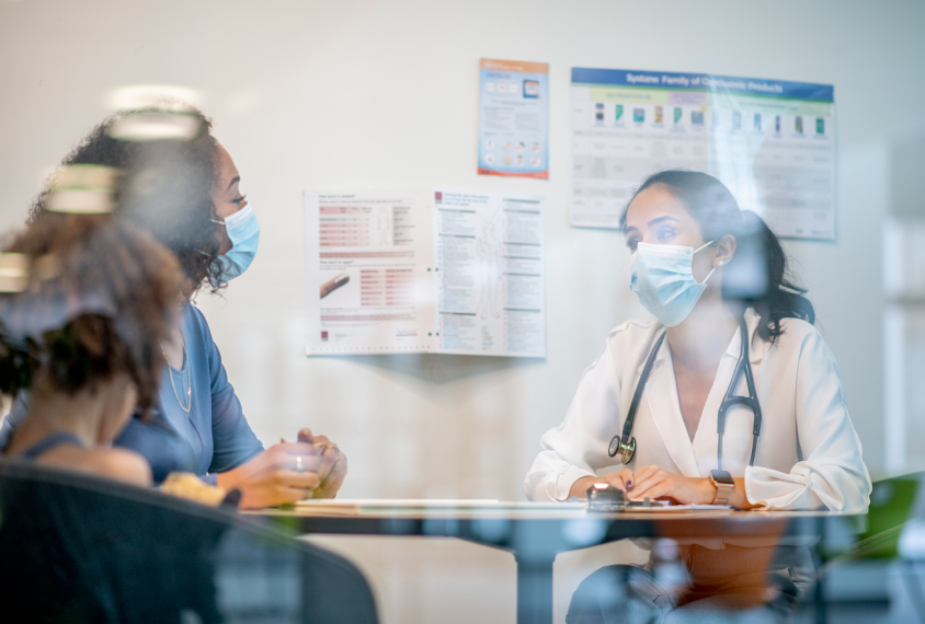 People in a medical office, seen through a window with reflections.