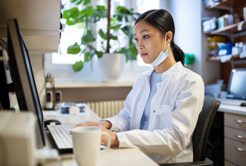 A woman in a lab coat types at a computer.