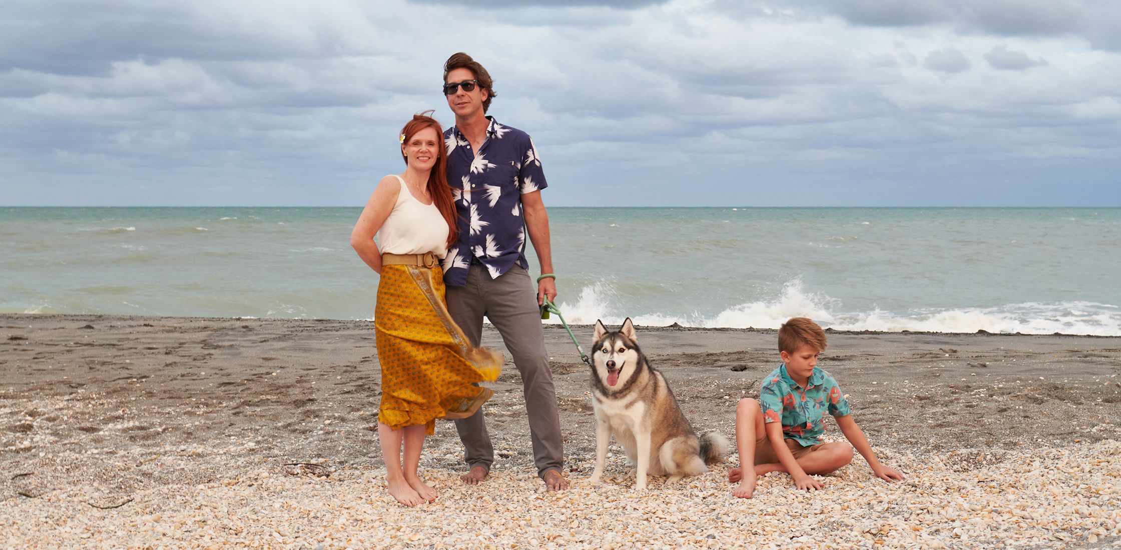 Gavin Rumbaugh stands on a beach with his family: his wife, dog and child.