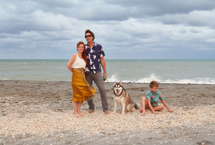 Gavin Rumbaugh stands on a beach with his family: his wife, dog and child.