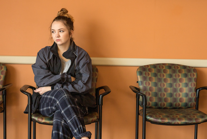 A young woman sits alone in a doctor’s office.