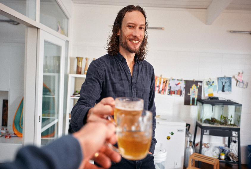 Graham Diering clinks drinking glasses with the photographer, as seen from the photographer’s point of view.