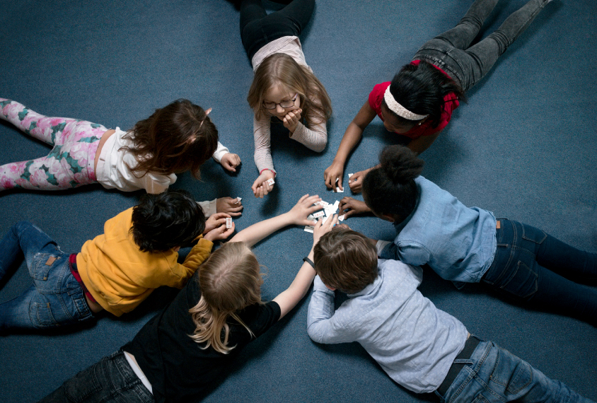 Overhead picture of a racially diverse group of children playing while lying on a blue carpet.