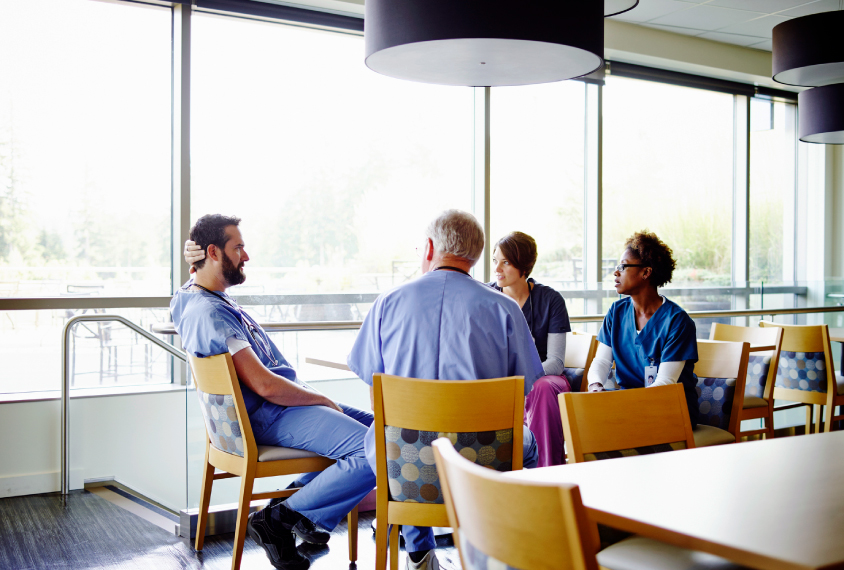 A group of doctors sit and talk in a hospital lounge.