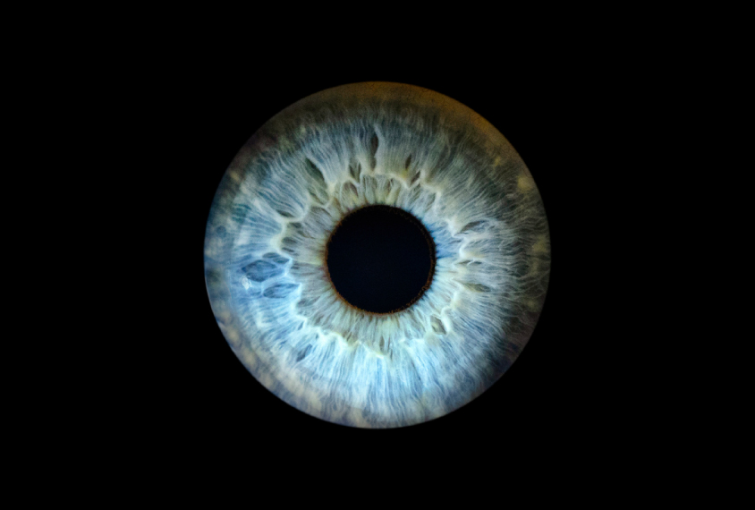 Close-up photograph of a blue iris and pupil against a black background.