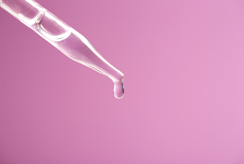 Drop of liquid medicine with air bubbles is dripping from a pipette on a light pink background.