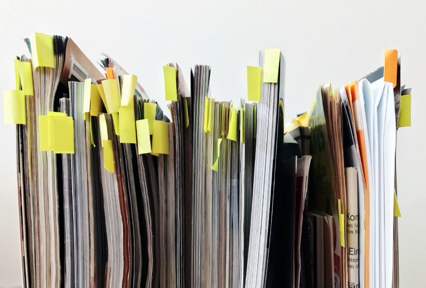 A row of magazines against the wall with many adhesive notes stuck between their pages.