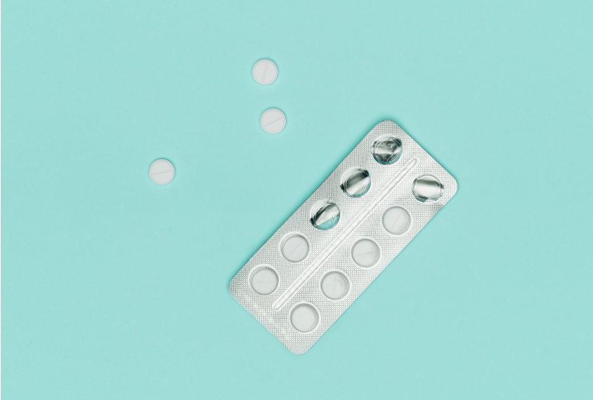 Photograph of white pills and blister pack on blue pastel colored background.