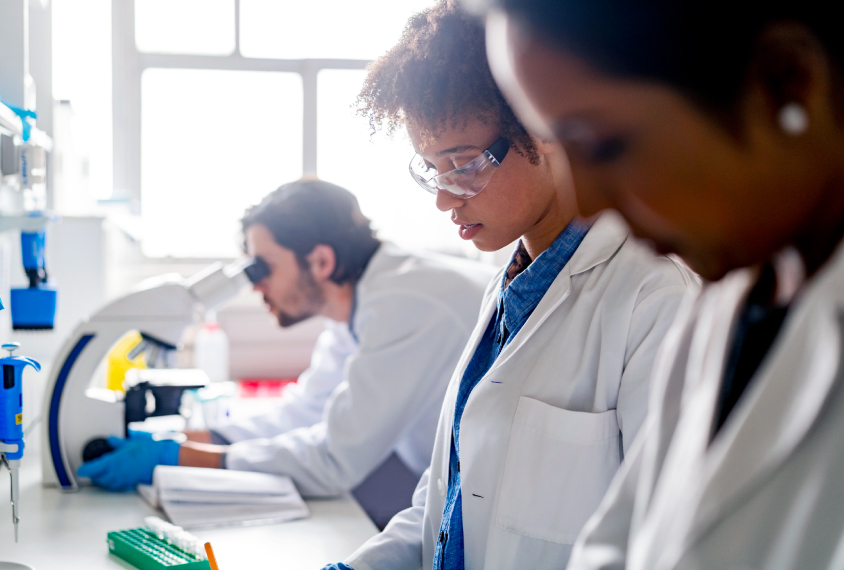 Photograph of two women of color working with a white male colleague in a laboratory.