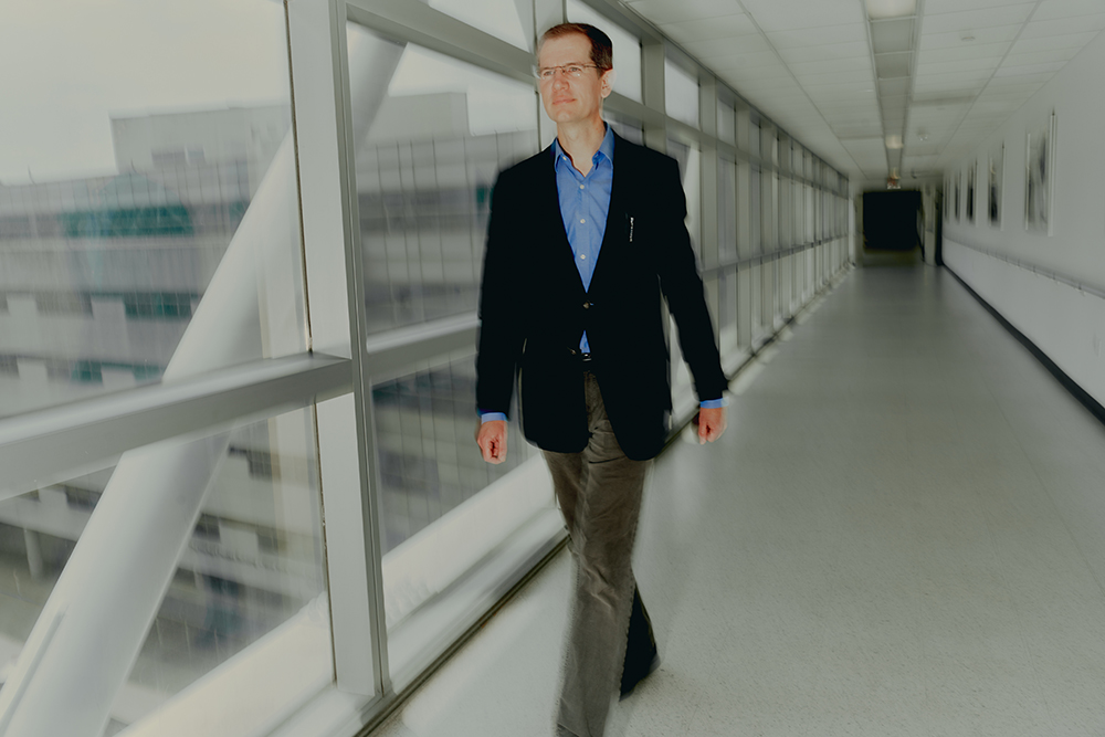 Jeremy Veenstra-VanderWeele walking in a windowed hall at Columbia University.