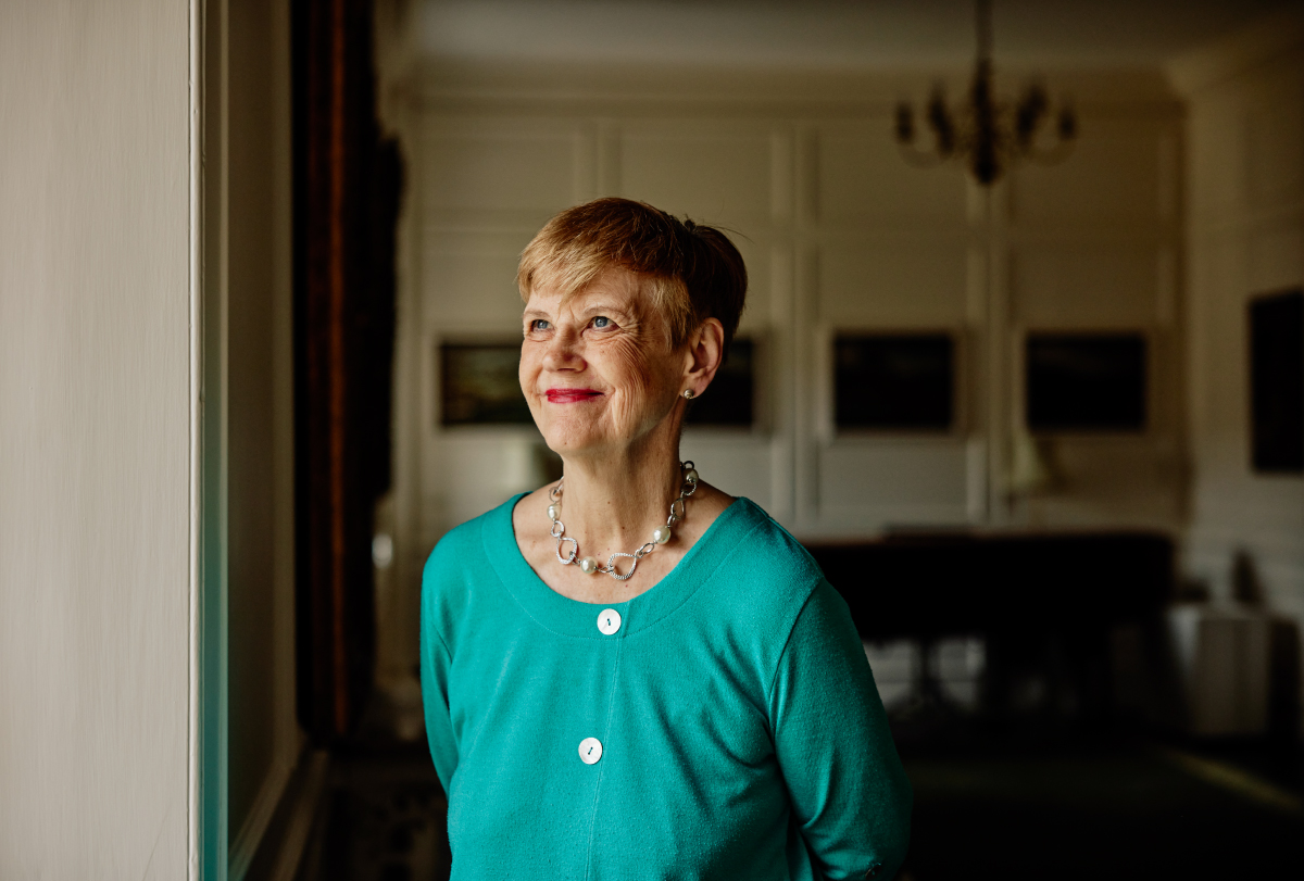 Dorothy Bishop stands in a dark room wearing a turquoise shirt.