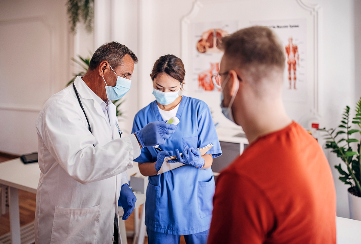 Photograph of a doctor and nurse checking a patient’s temperature and taking notes.