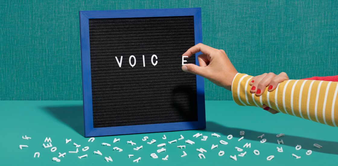 An illustration of a hand placing letters spelling the word voice on a black board.