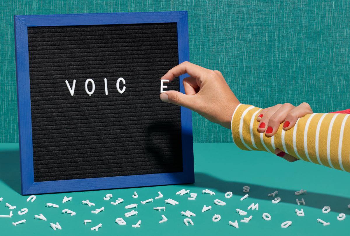 An illustration of a hand placing letters spelling the word voice on a black board.