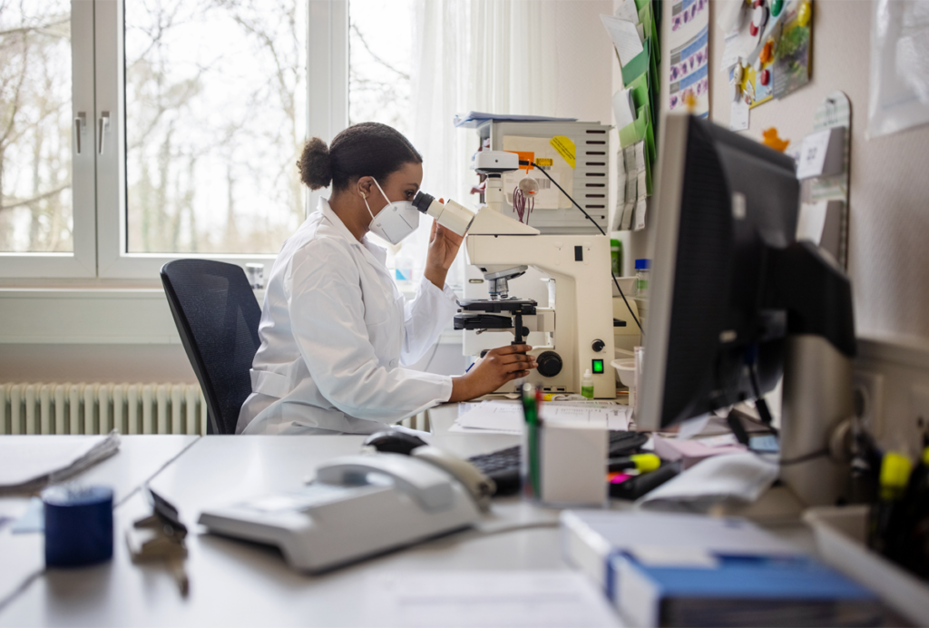 A scientist in a white coat uses a microscope in a lab.