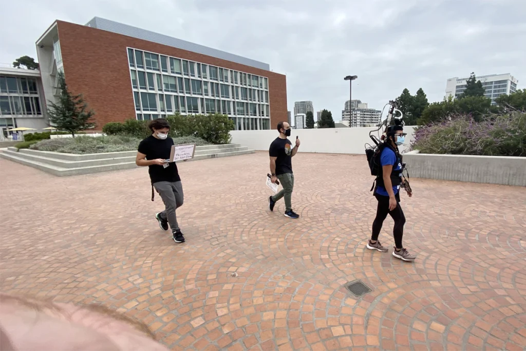 Three researchers, one wearing movement-tracking devices, walk around a university campus.