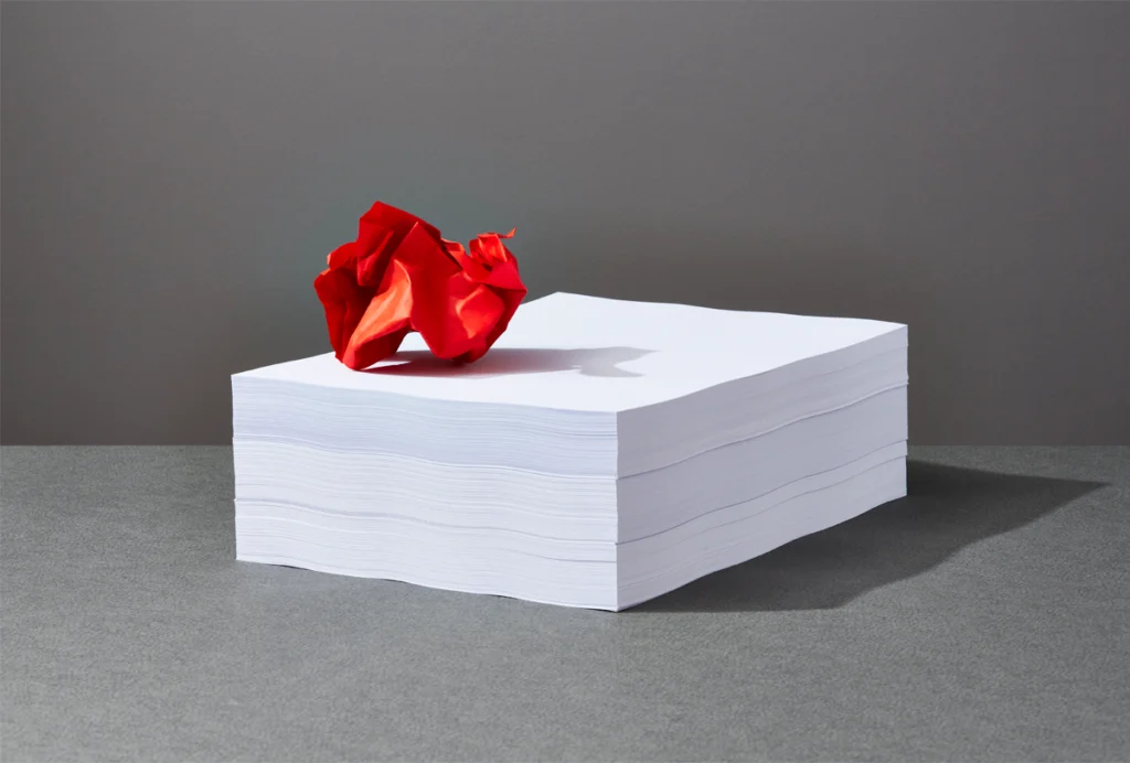 A crumpled piece of paper atop a stack of papers against a grey background.
