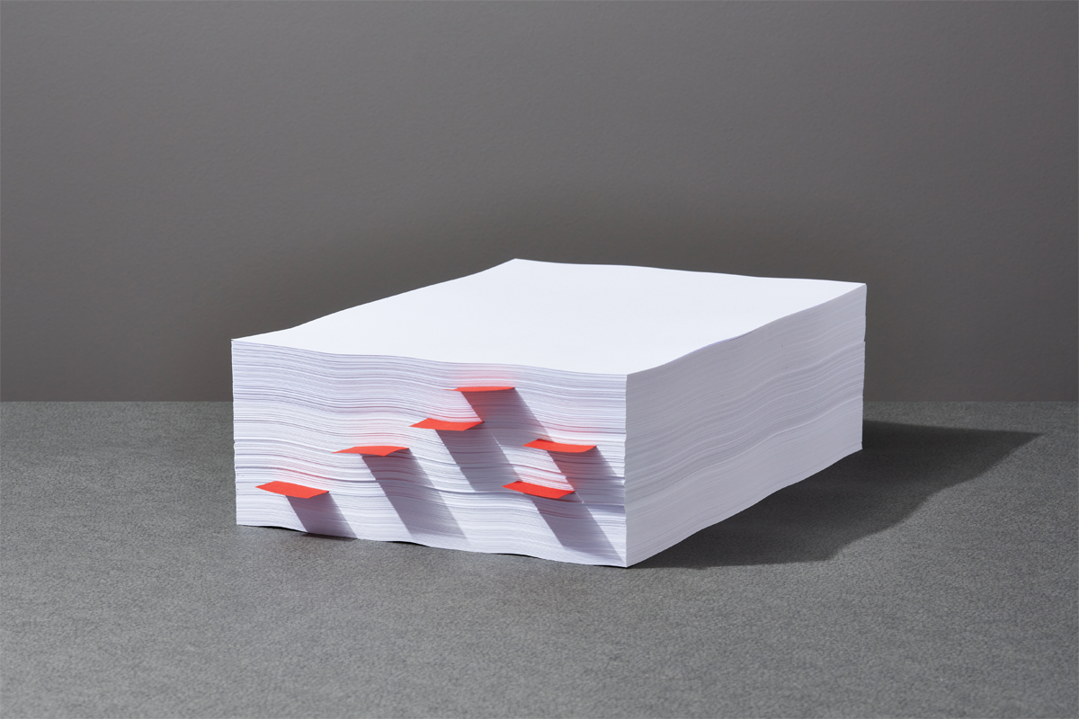 Photograph of a stack of white papers with six red post-it notes sticking out.
