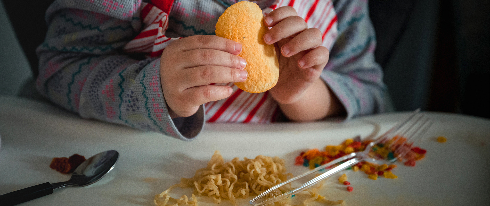 Coraline holds a chip in her highchair, where she has organized her food into groups.